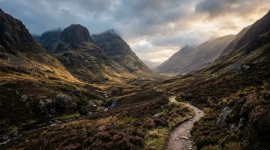 Misty Scottish Highland glen with winding path through dramatic mountain landscape at golden hour