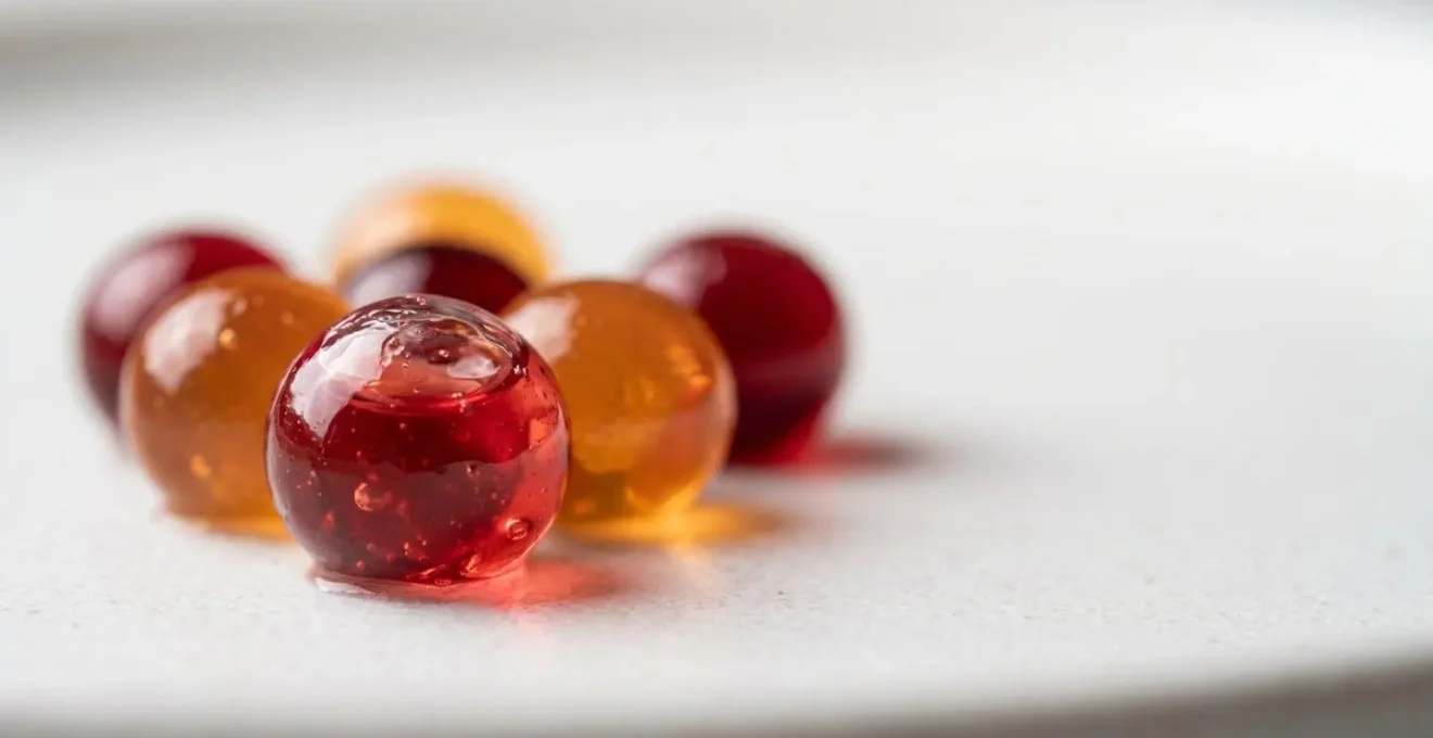 Extreme close-up of glossy translucent fruit caviar pearls on white ceramic surface